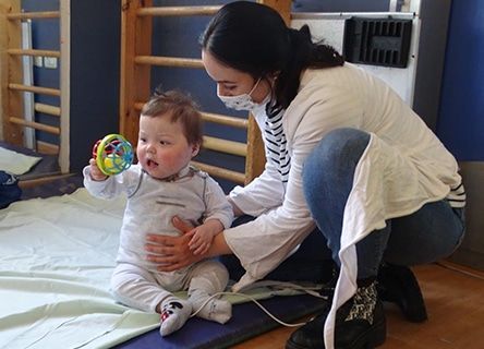 A woman is kneeling down next to a baby holding a toy.