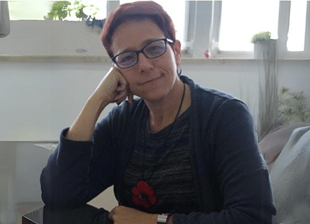 A woman wearing glasses is sitting at a table with her hand on her chin.