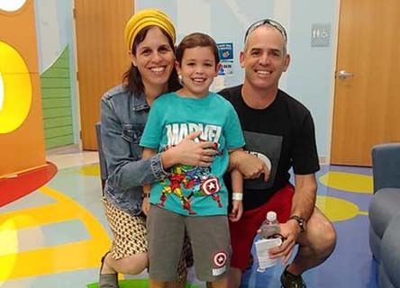 A man and woman are posing for a picture with a little boy wearing a marvel shirt.