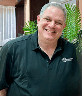 A man in a black shirt is smiling in front of a palm tree.