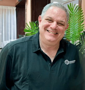 A man in a black shirt is smiling in front of a palm tree.