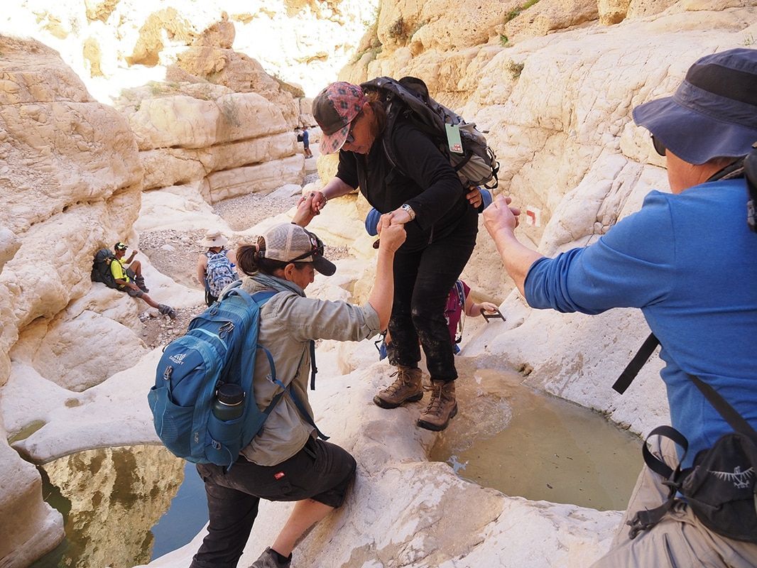 A group of people are helping each other climb a rocky cliff.