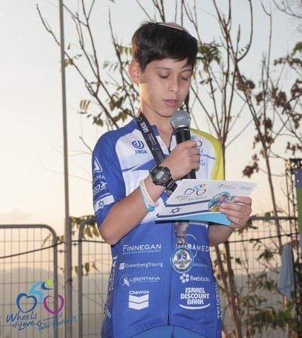 A young boy wearing a medal is holding a microphone and reading a book.