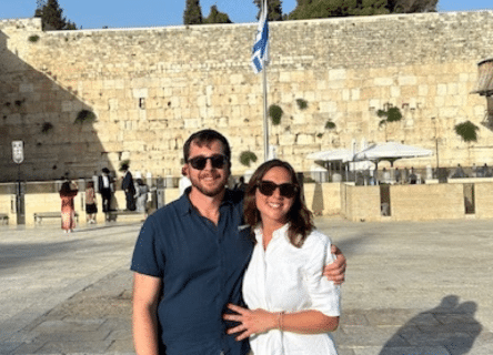 A man and a woman are posing for a picture in front of the western wall.
