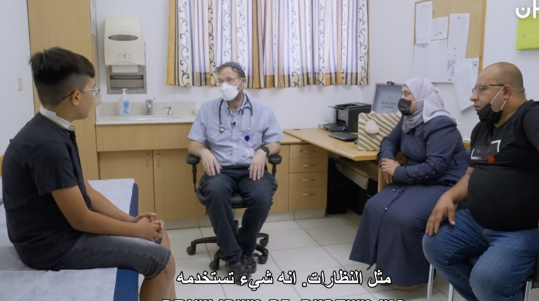 A group of people are sitting around a doctor who is wearing a mask.