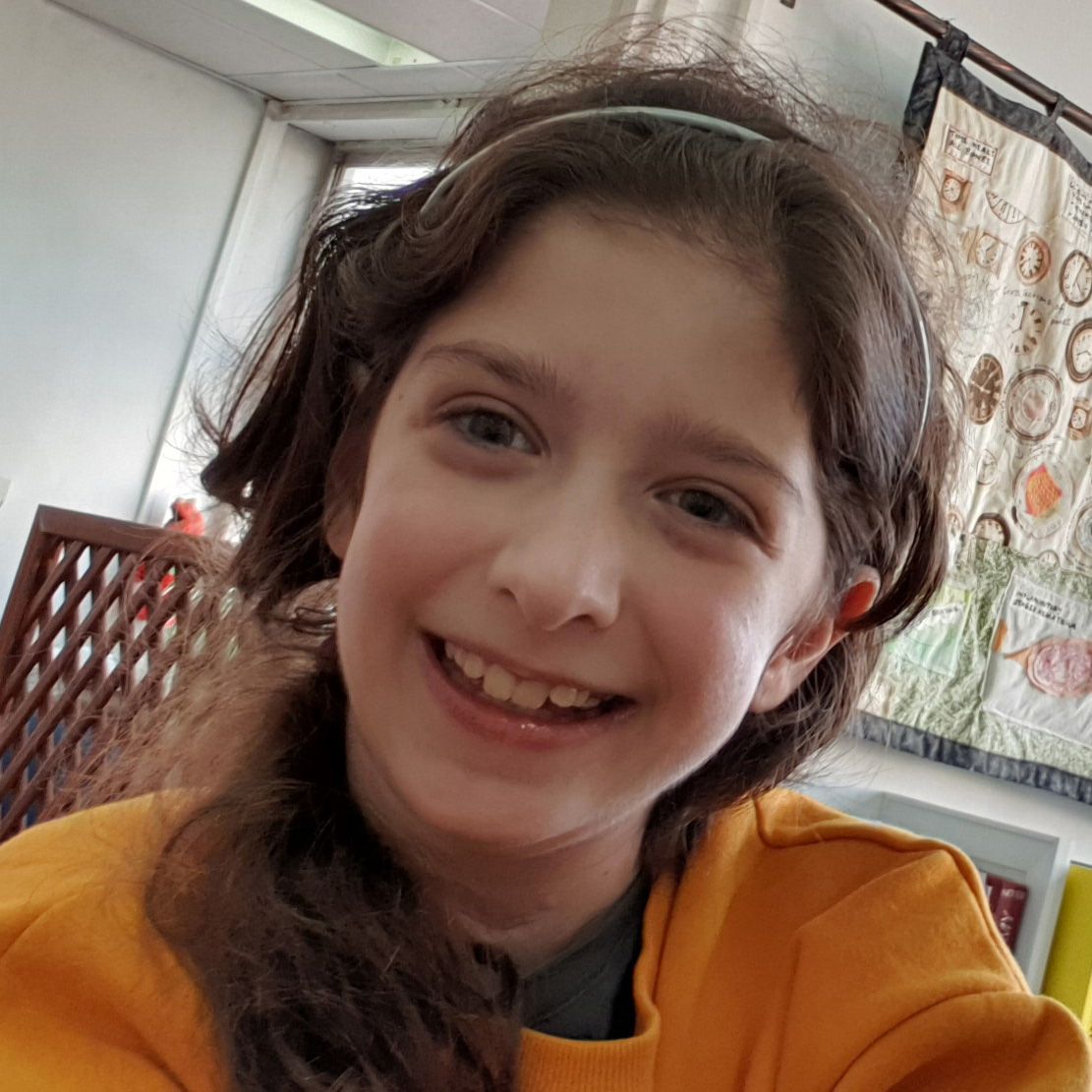A young girl wearing a yellow sweatshirt is smiling for the camera.