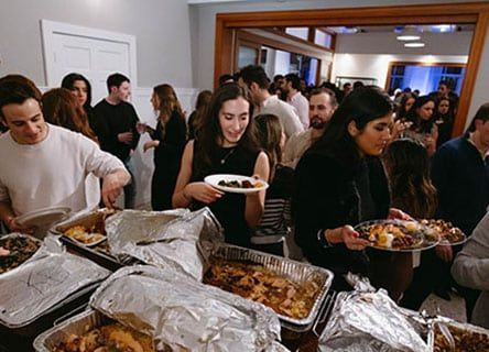 A group of people are standing around a table eating food.