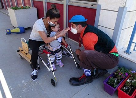 A clown is helping a little girl with a walker.