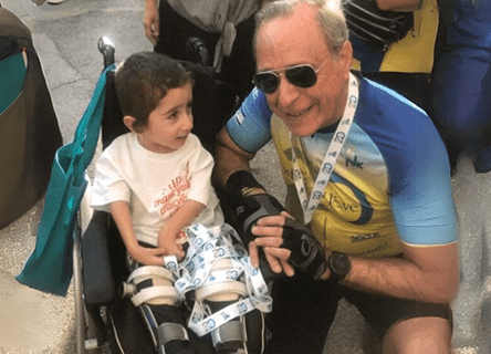 A man is kneeling down next to a child in a wheelchair.