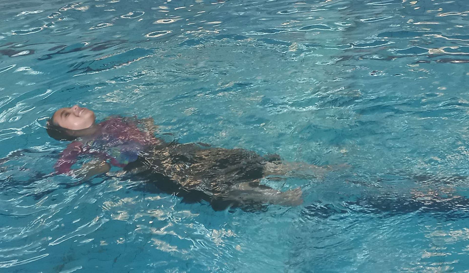 A person is floating on their back in a swimming pool.