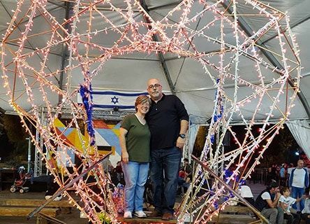 A man and a woman are posing for a picture in front of a heart made of lights.