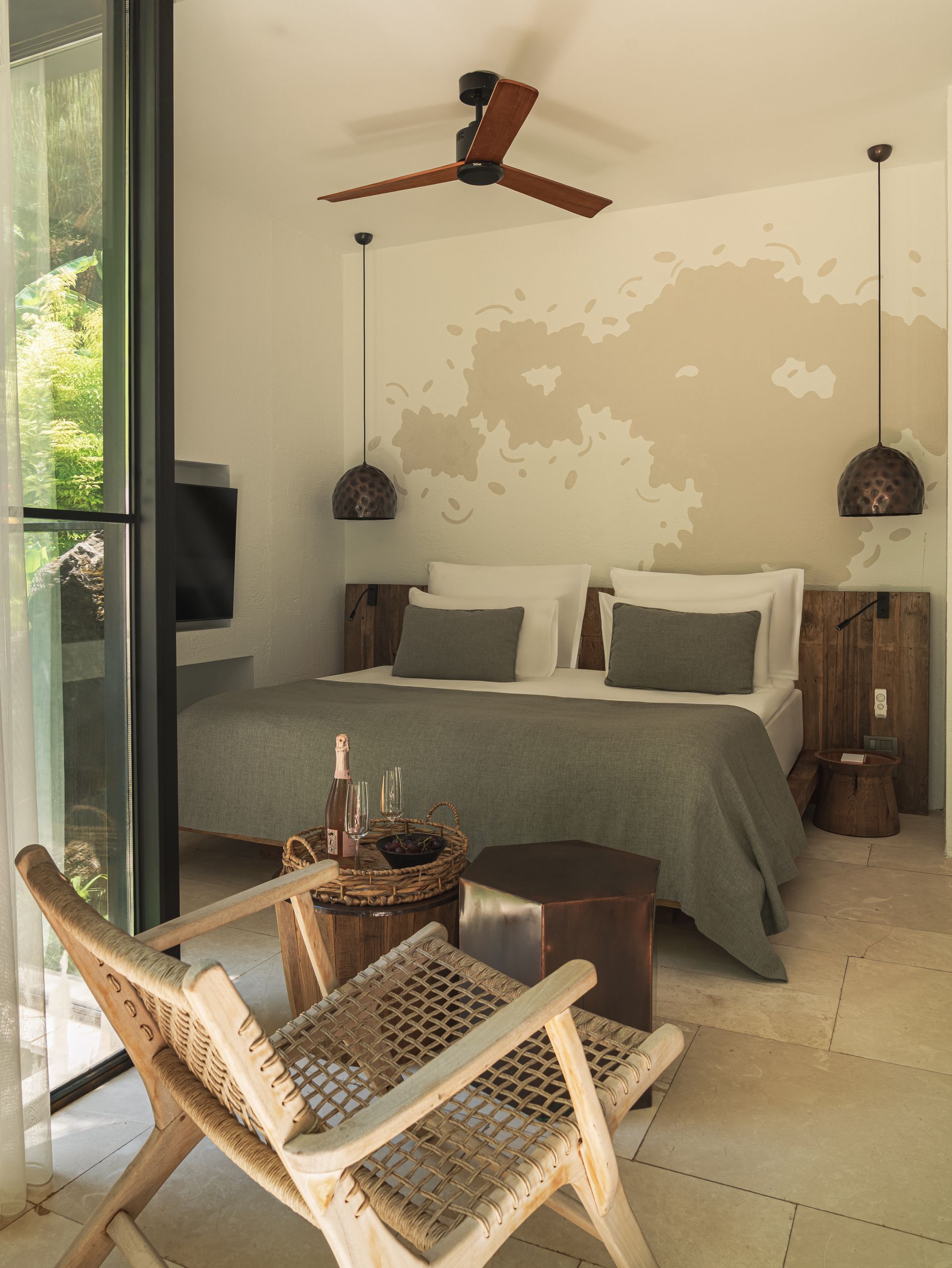 Modern, minimalist bedroom with a bed, textured wall art, pendant lighting, and a wooden chair in the foreground.