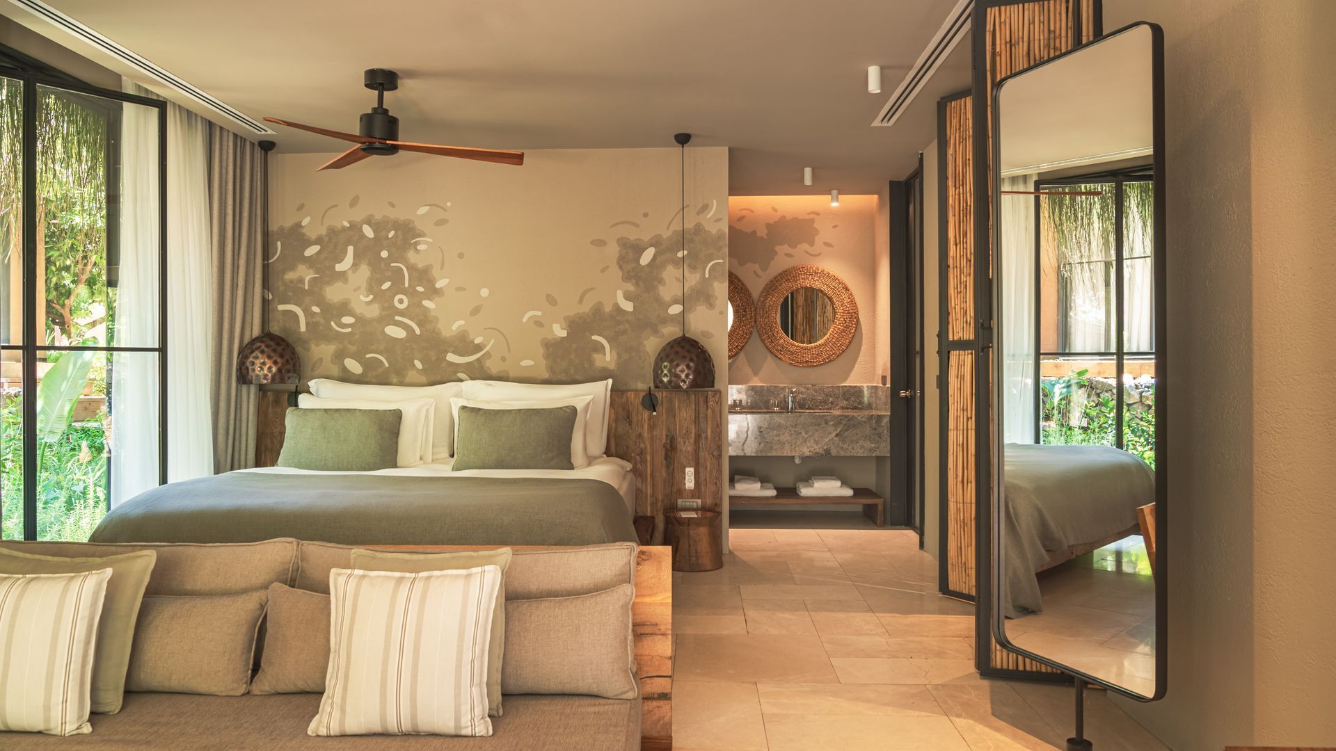 A modern hotel bedroom with a plush bed, neutral decor, a ceiling fan, and a large floor mirror reflecting the space.