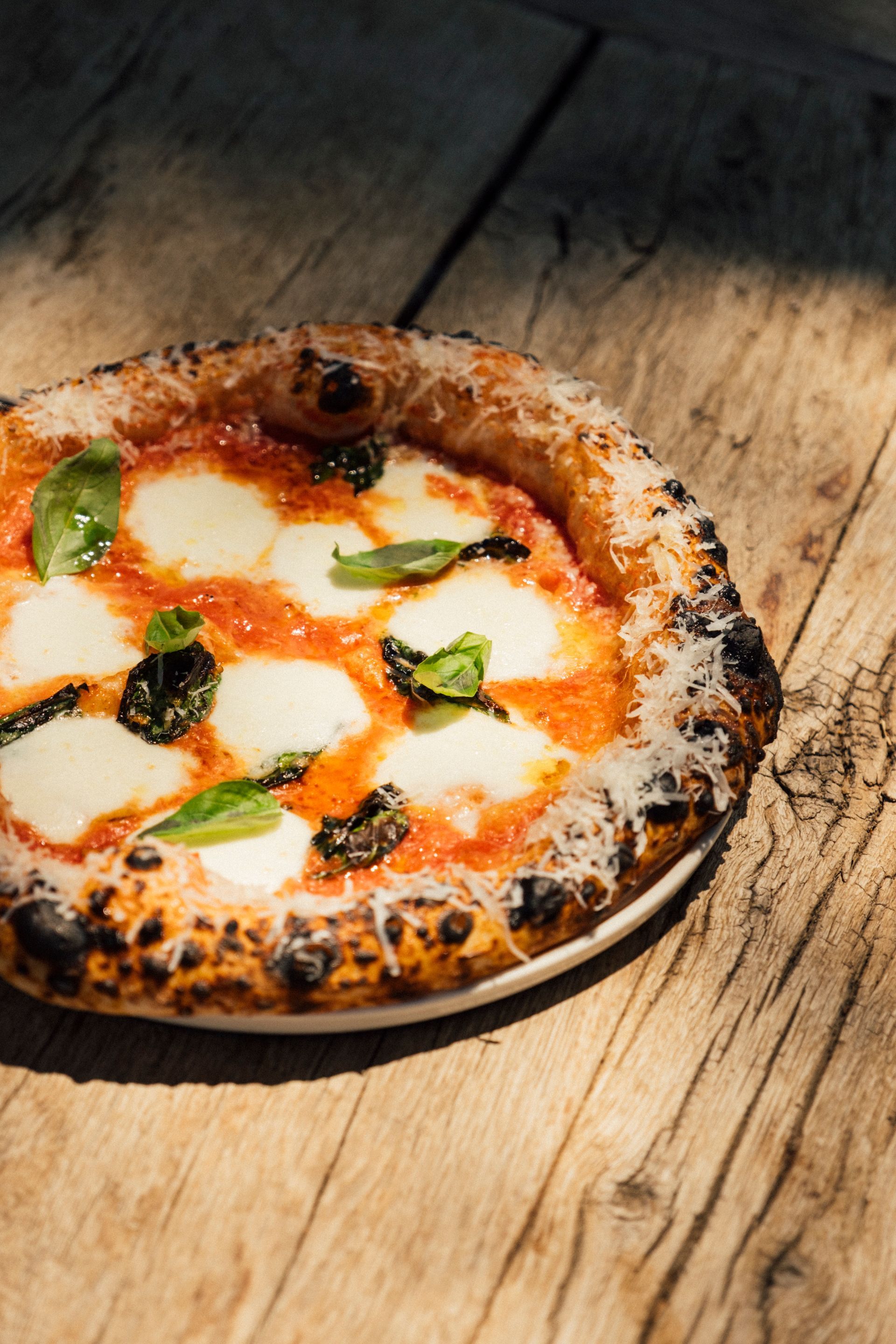 A freshly baked Margherita pizza with mozzarella, tomato sauce, and basil on a white plate atop a rustic wooden table.