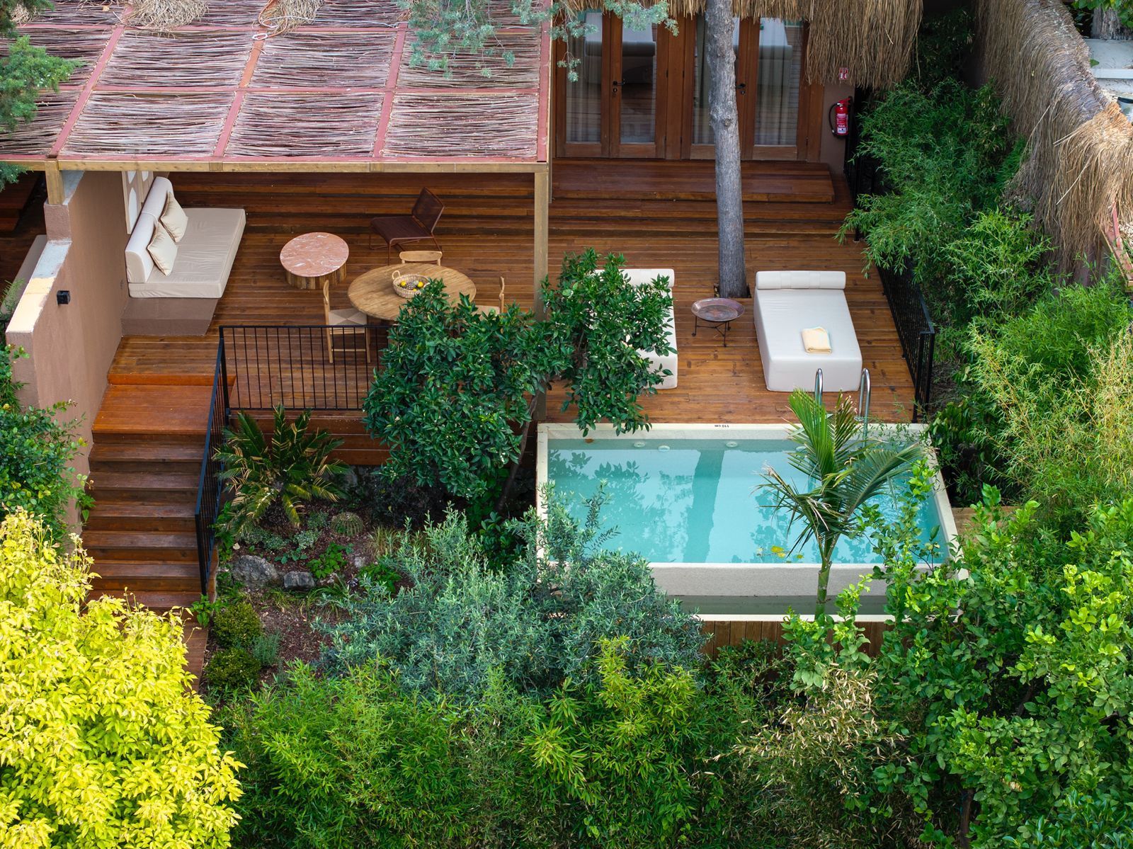 A private villa deck with a swimming pool, lounge seating, and wooden patio, surrounded by lush trees and greenery.