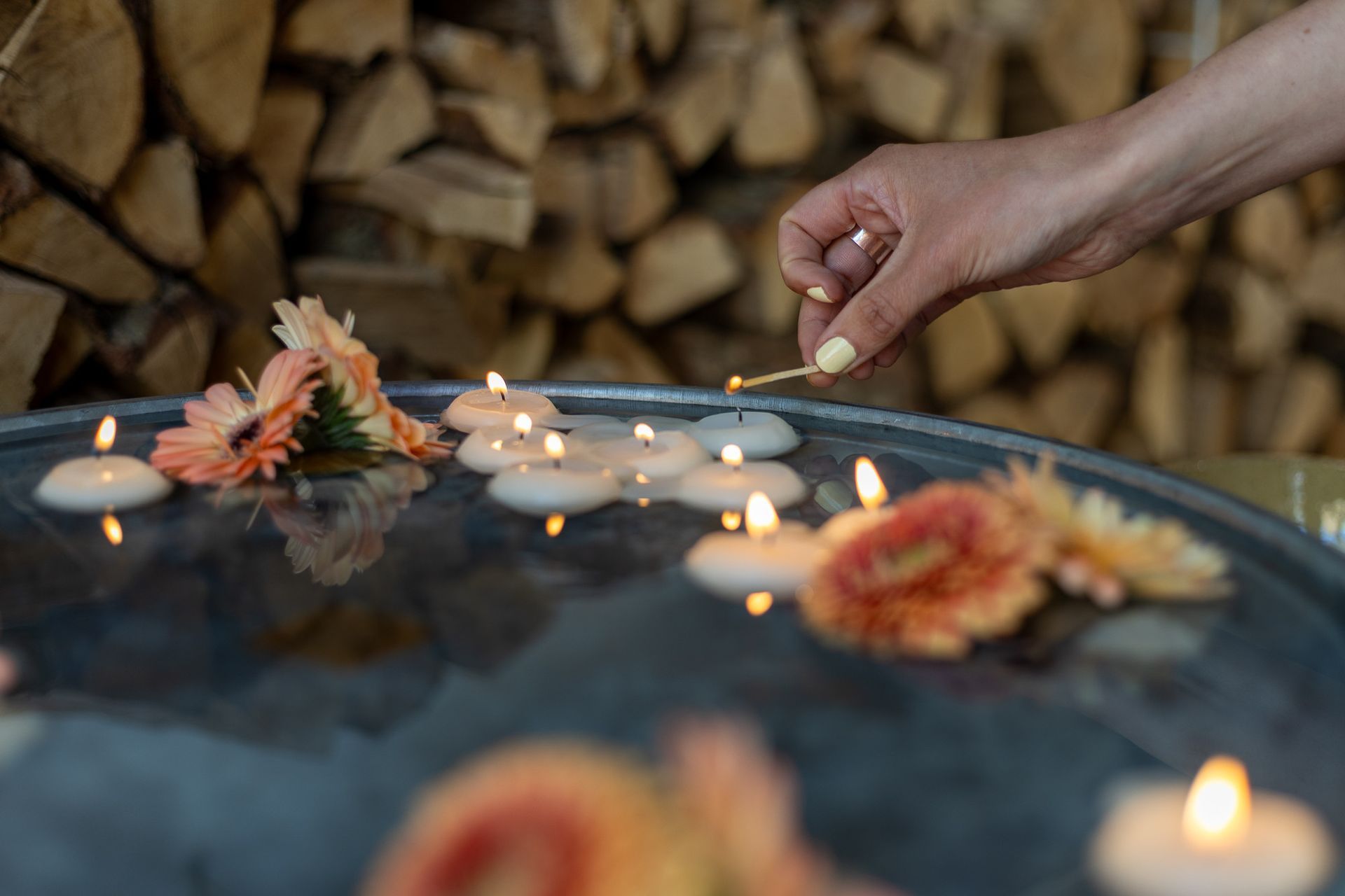Hand steekt een drijvende kaars tussen drijvende bloemen aan.