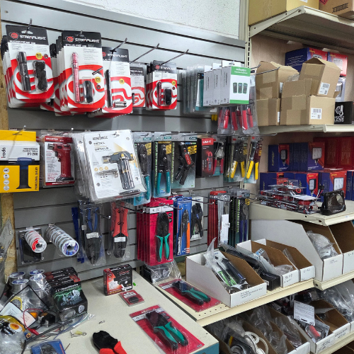 Hardware store aisle with hanging tools, cables, and boxed parts on shelves.