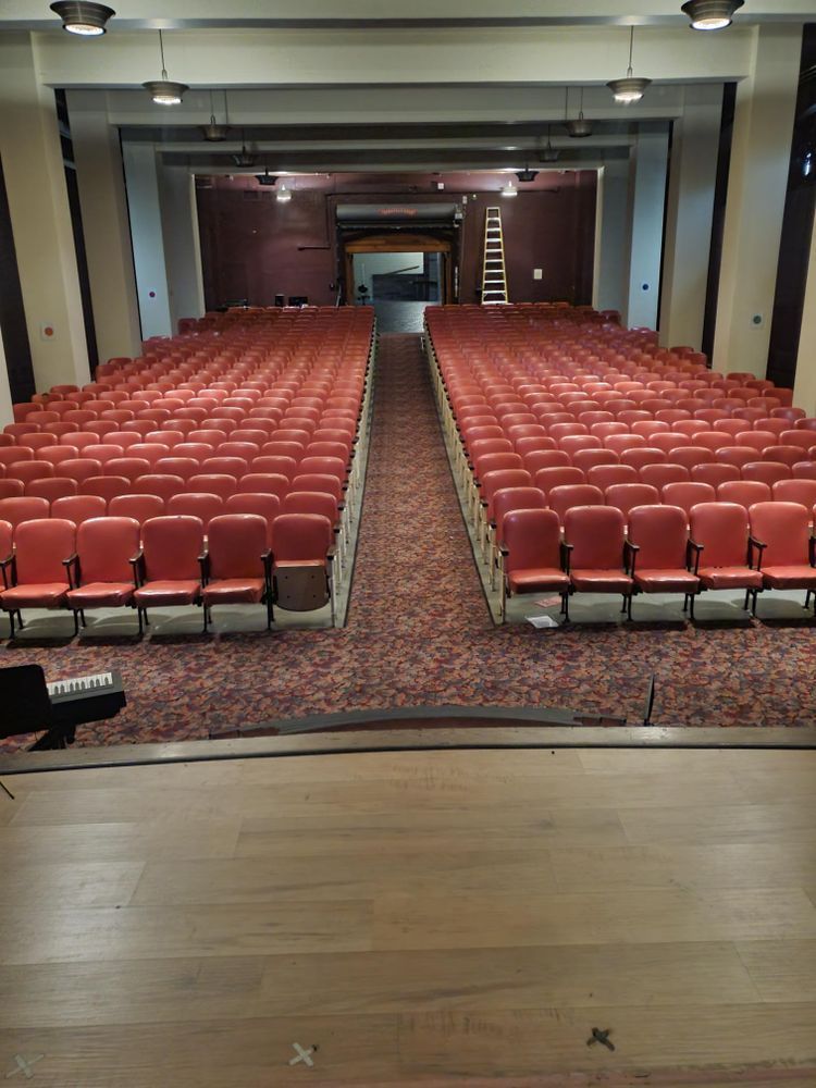 A large auditorium with rows of red chairs and a ladder