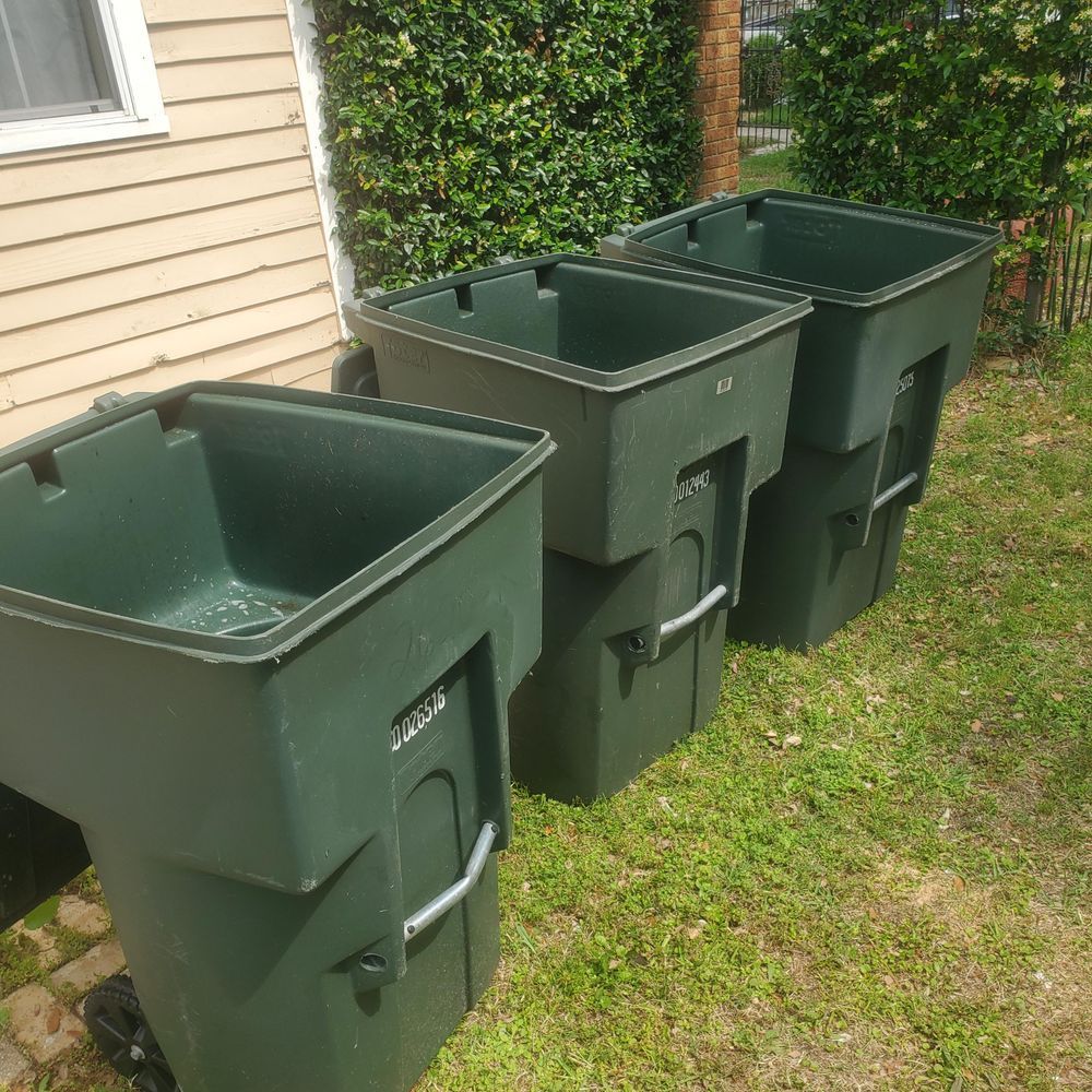 Three green garbage cans are sitting in the grass in front of a house