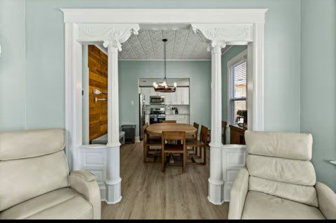 Two cream recliners face an ornate doorway leading to a dining room with a table, chairs, and kitchen.