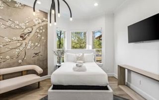 Bedroom with a floral wall mural, white bed, a small sofa, a large TV, and a modern light fixture.