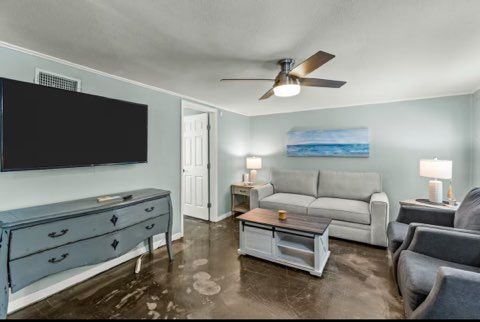 Living room with TV, gray sofa, blue accent wall, coffee table, and ceiling fan.