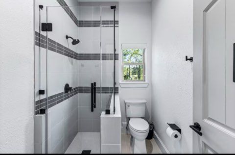 Bathroom with glass shower, white toilet, and black fixtures; gray tiled wall accent.
