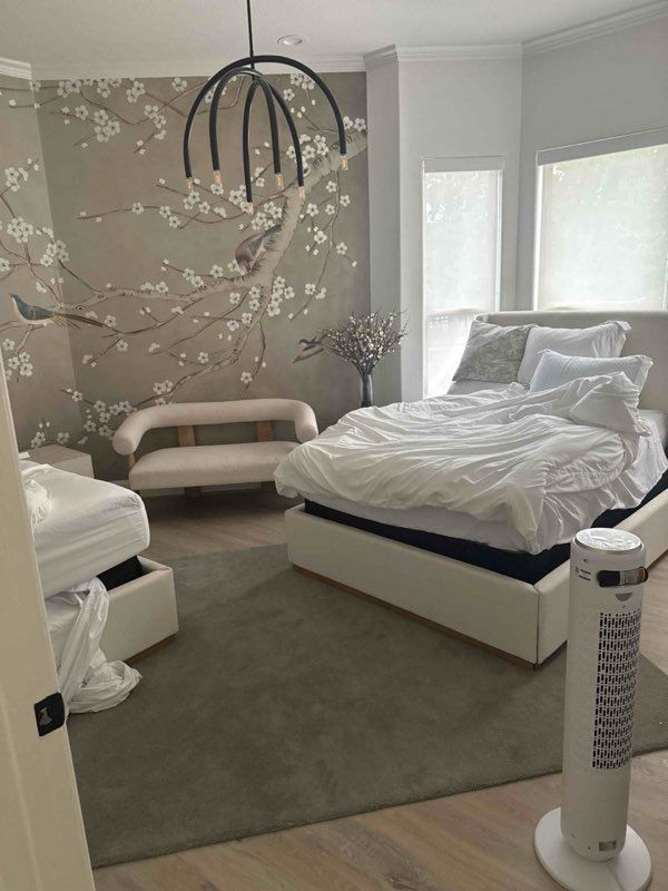 Bedroom with bed, loveseat, floral wall design, and cooling fan. Neutral tones and natural light.