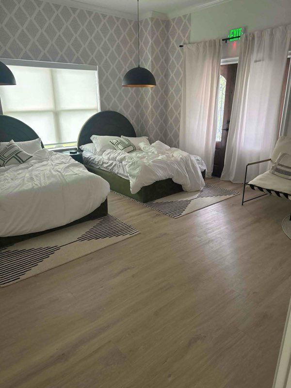 Two beds in a room, light wood floors, diamond wallpaper, black pendant lights, white curtains.