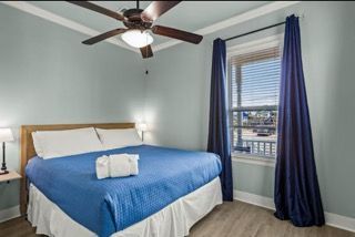 Bedroom with a blue bedspread, dark curtains, and a window with a view.