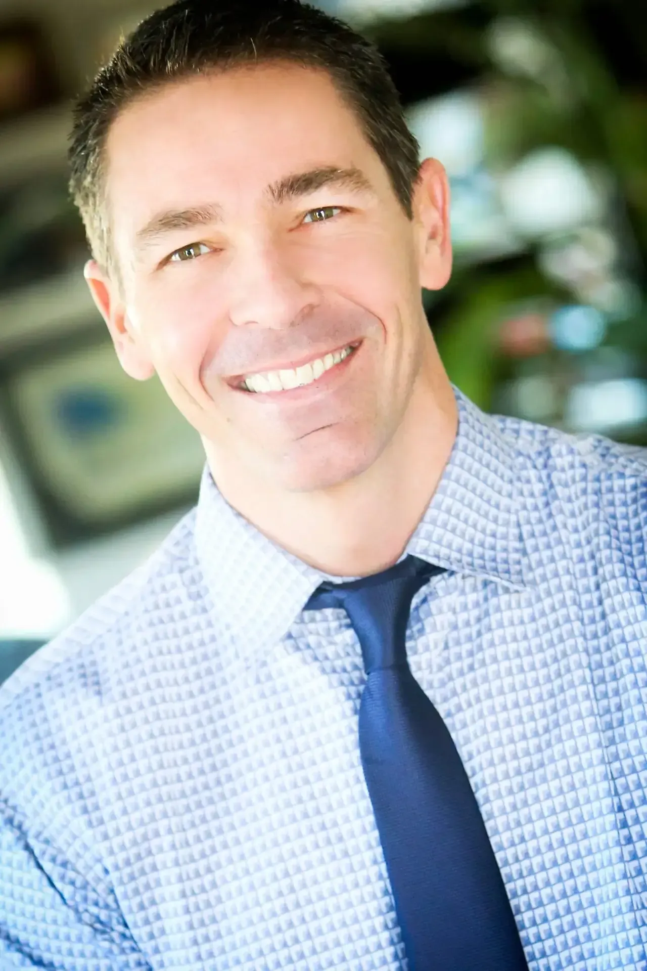 A man in a blue shirt and blue tie is smiling for the camera.