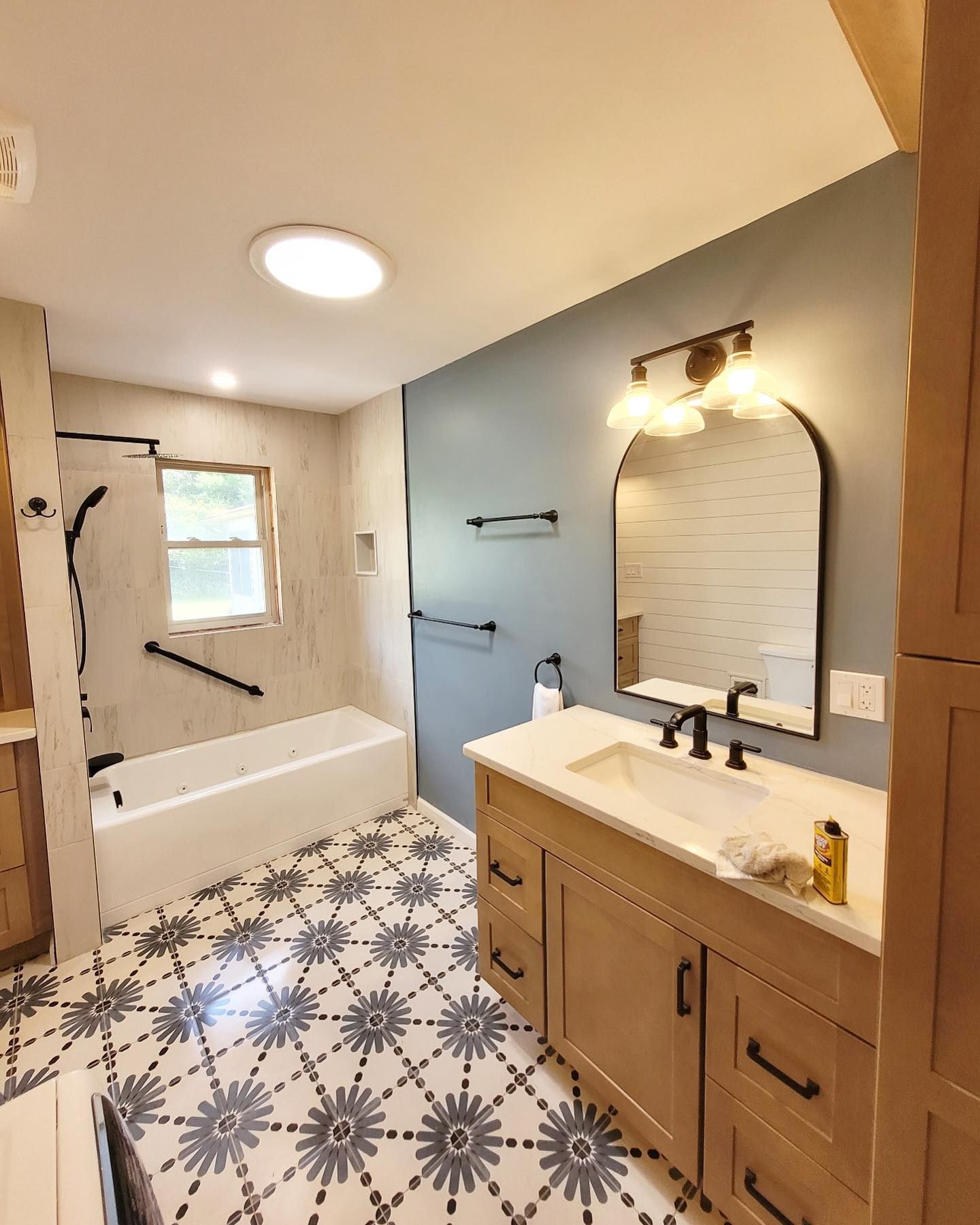 a blue and white bathroom with a sink , tub shower and mirror by WS Design & Build
