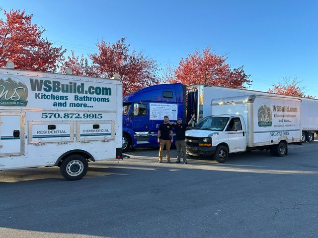 Two men standing in front of three WSBuild trucks. Autumn trees in the background.