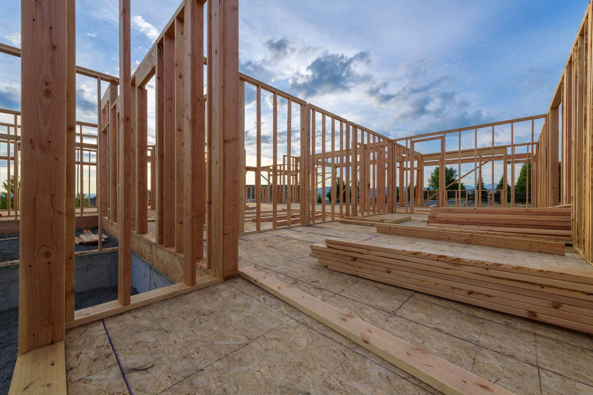 Framed house interior under construction with wooden studs, flooring, and open sky visible through walls