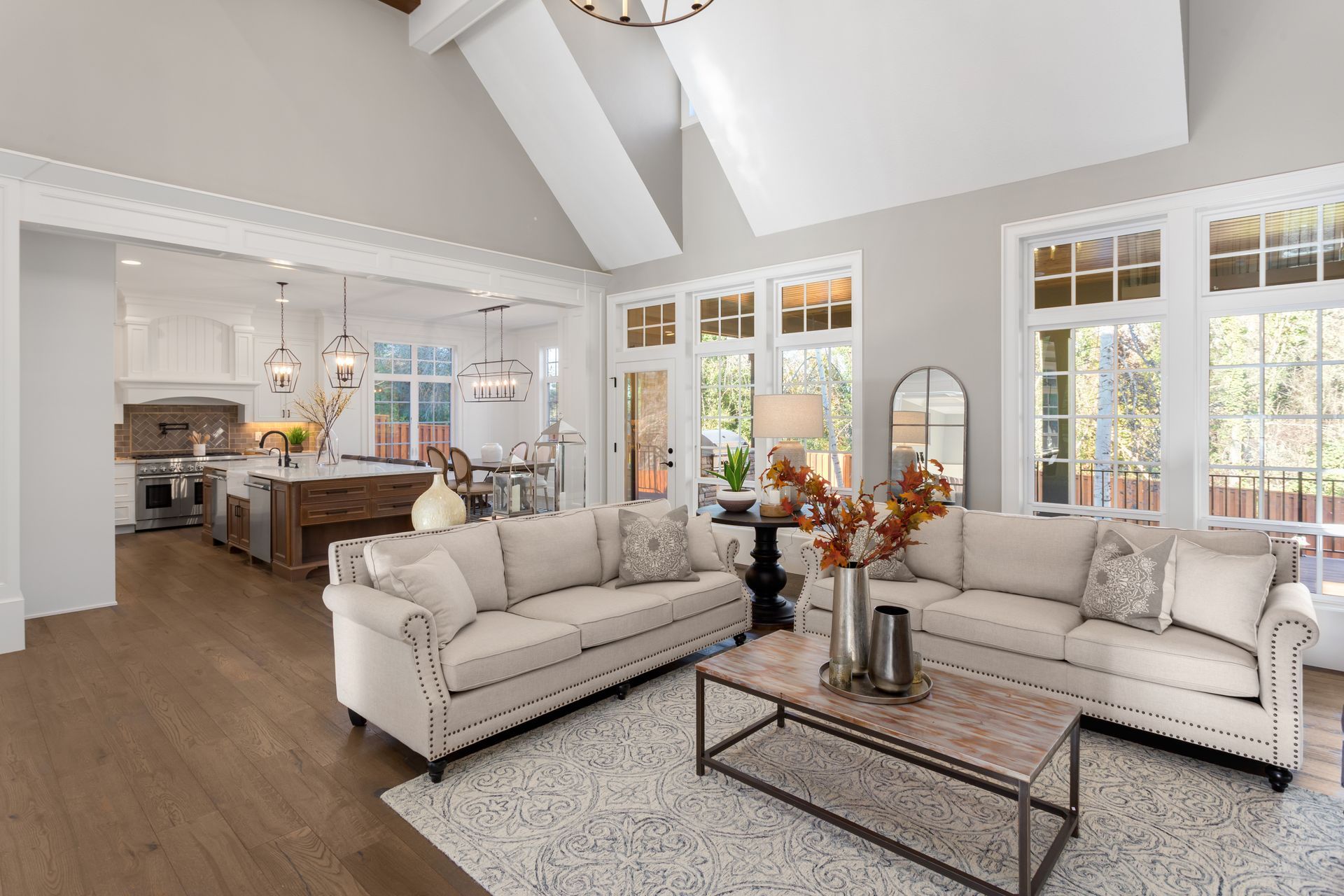 Bright open-concept living room with beige sofas, coffee table, and kitchen in the background