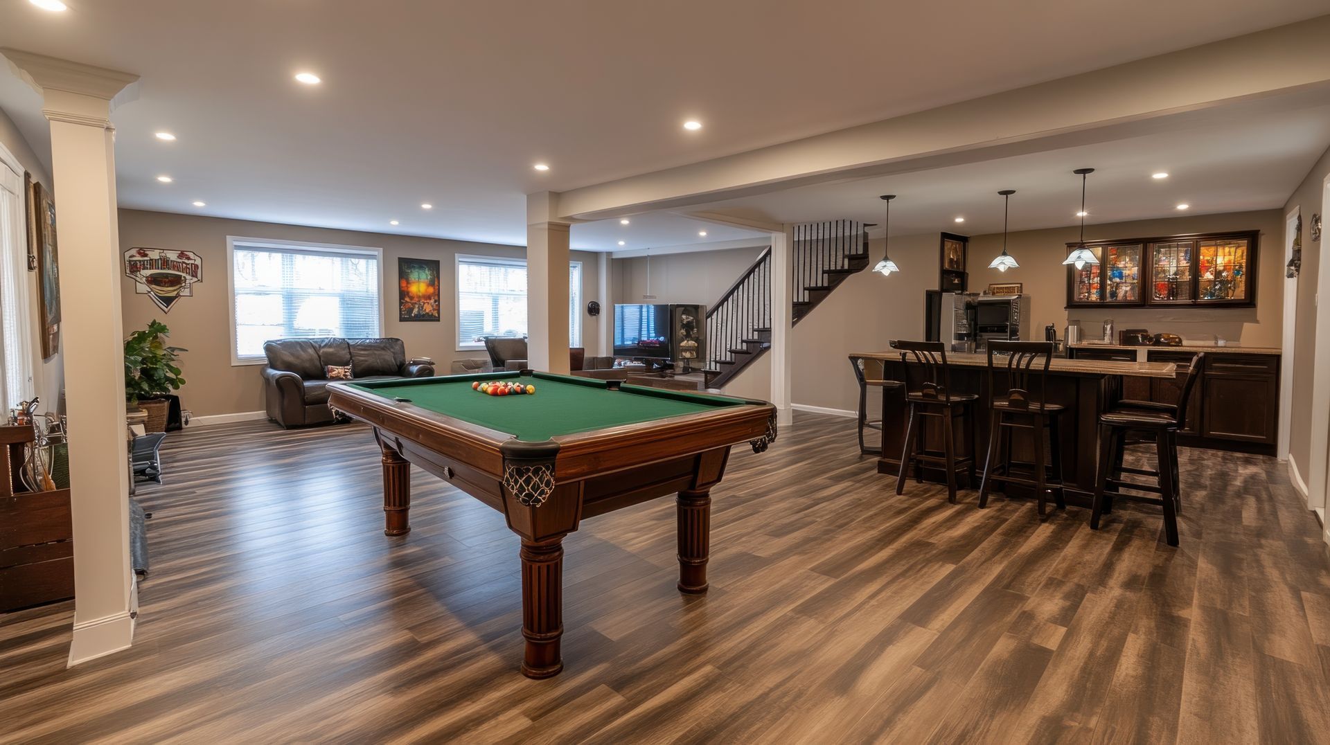 Spacious basement rec room with pool table, bar seating, wood floors, and stairs to upper level
