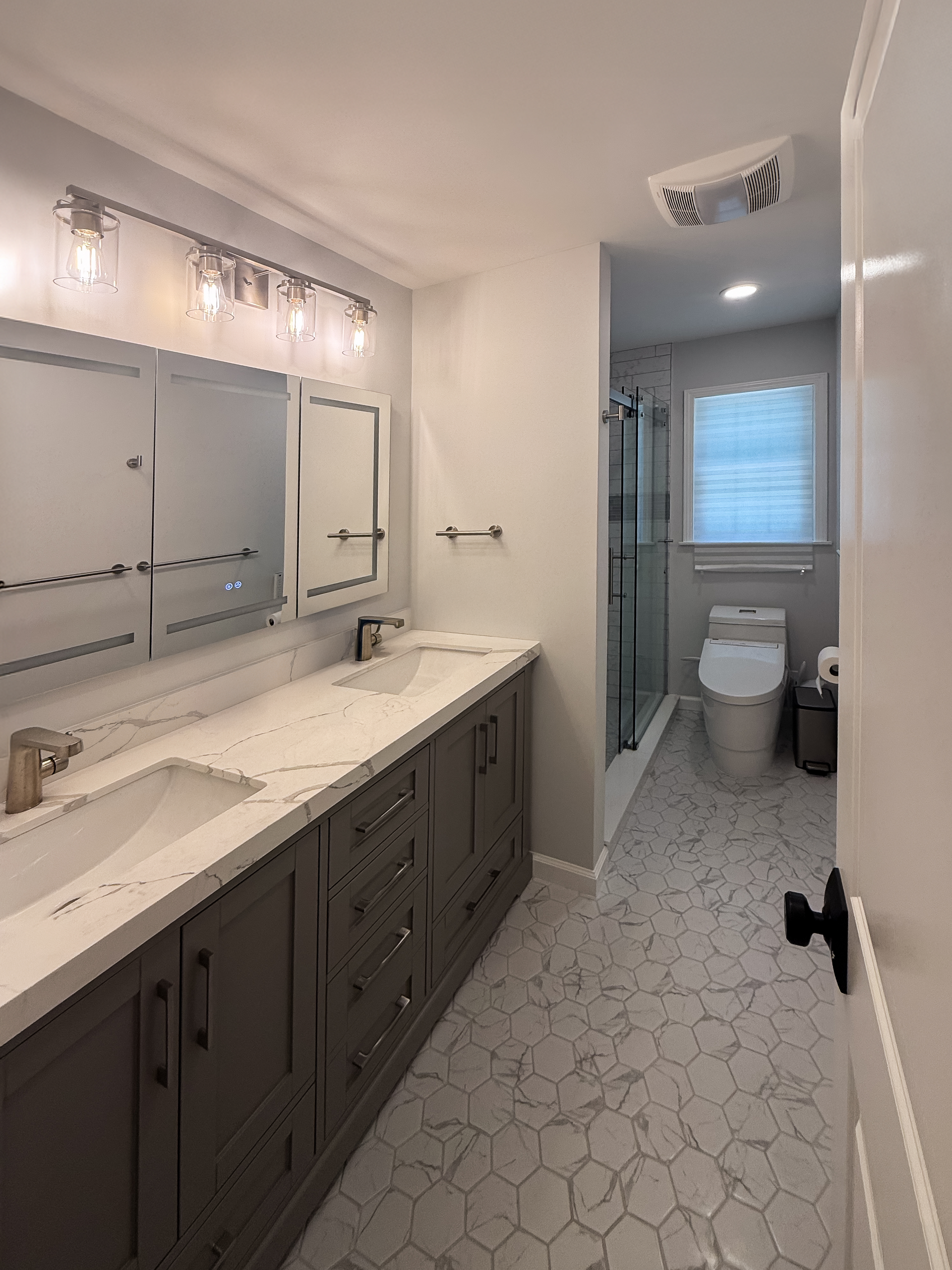 Modern bathroom with gray vanity, double sinks, and hexagon floor tiles.