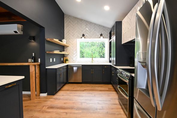 Modern black kitchen with stainless steel appliances, wood floor, and a window over the sink