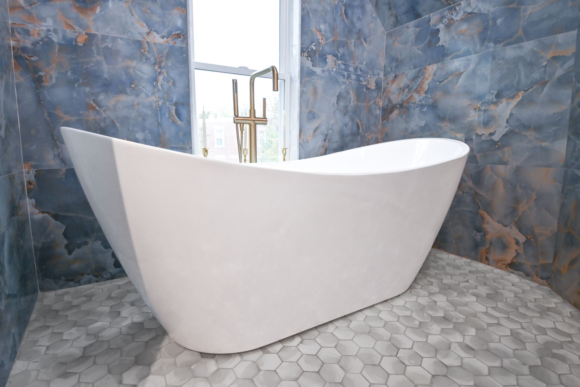 White bathtub in a bathroom with blue and gold tiled walls and a hexagon tile floor.