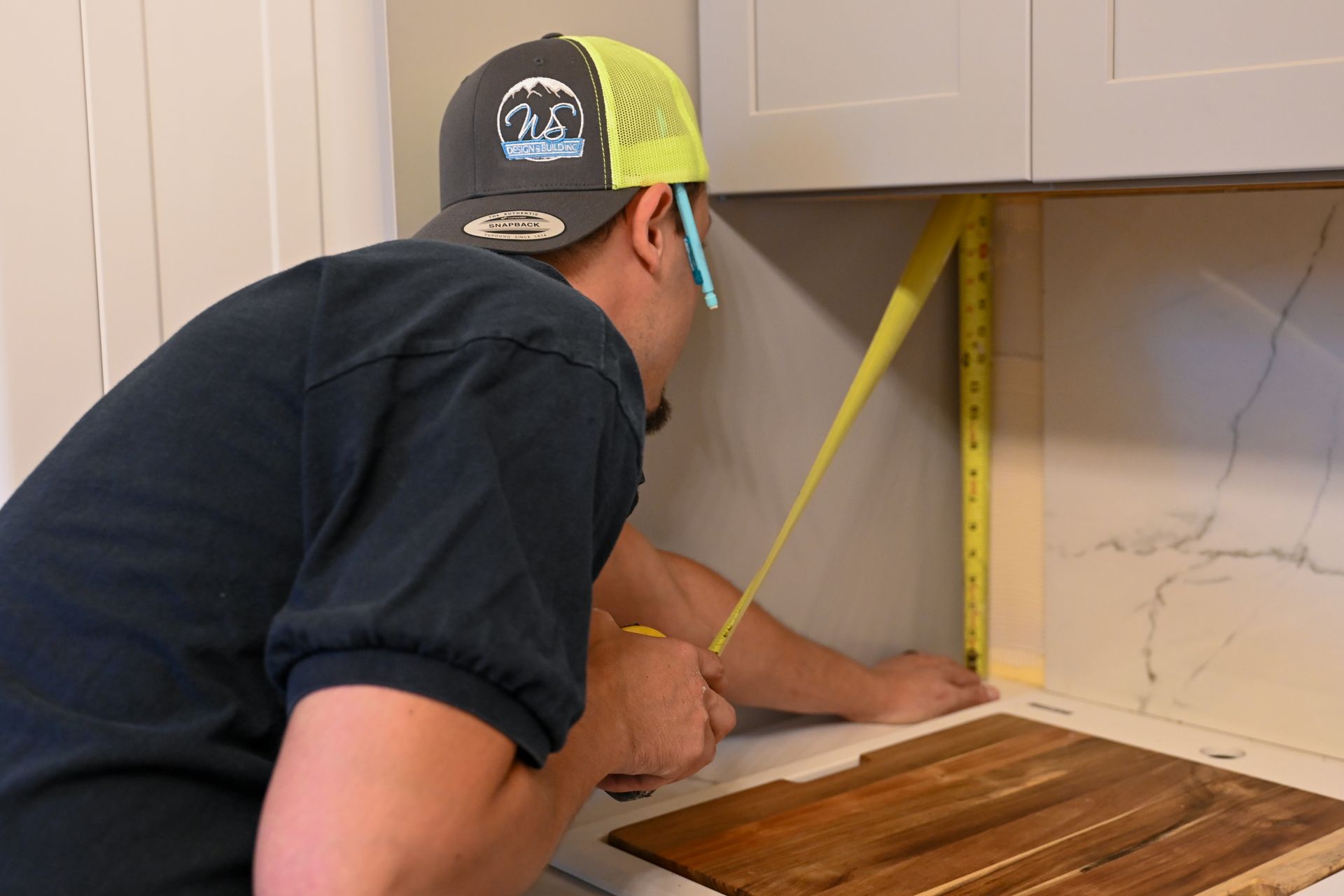 A man is measuring a piece of wood with a tape measure.