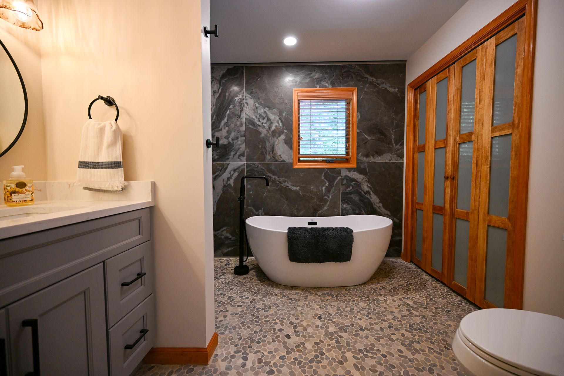 Bathroom with gray vanity, black fixtures, patterned floor, freestanding tub, and dark accent wall.