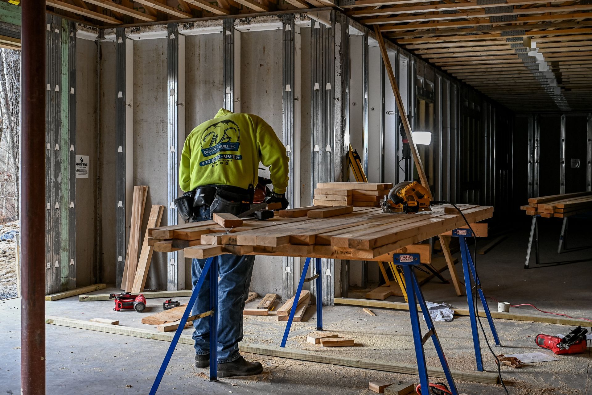 Construction worker using a saw on a wooden structure, inside a building.
