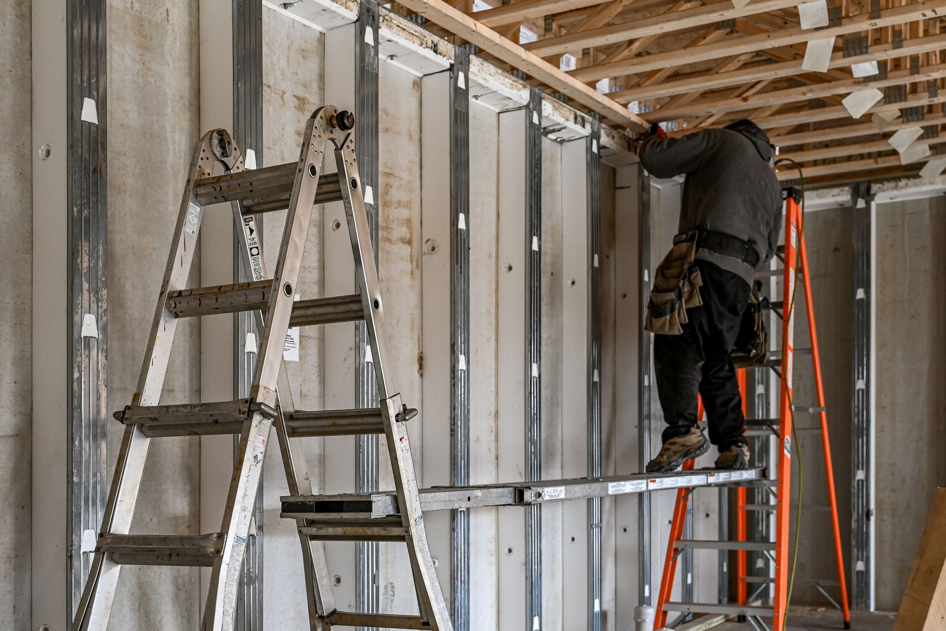 Construction worker on a ladder installing a wooden beam indoors.
