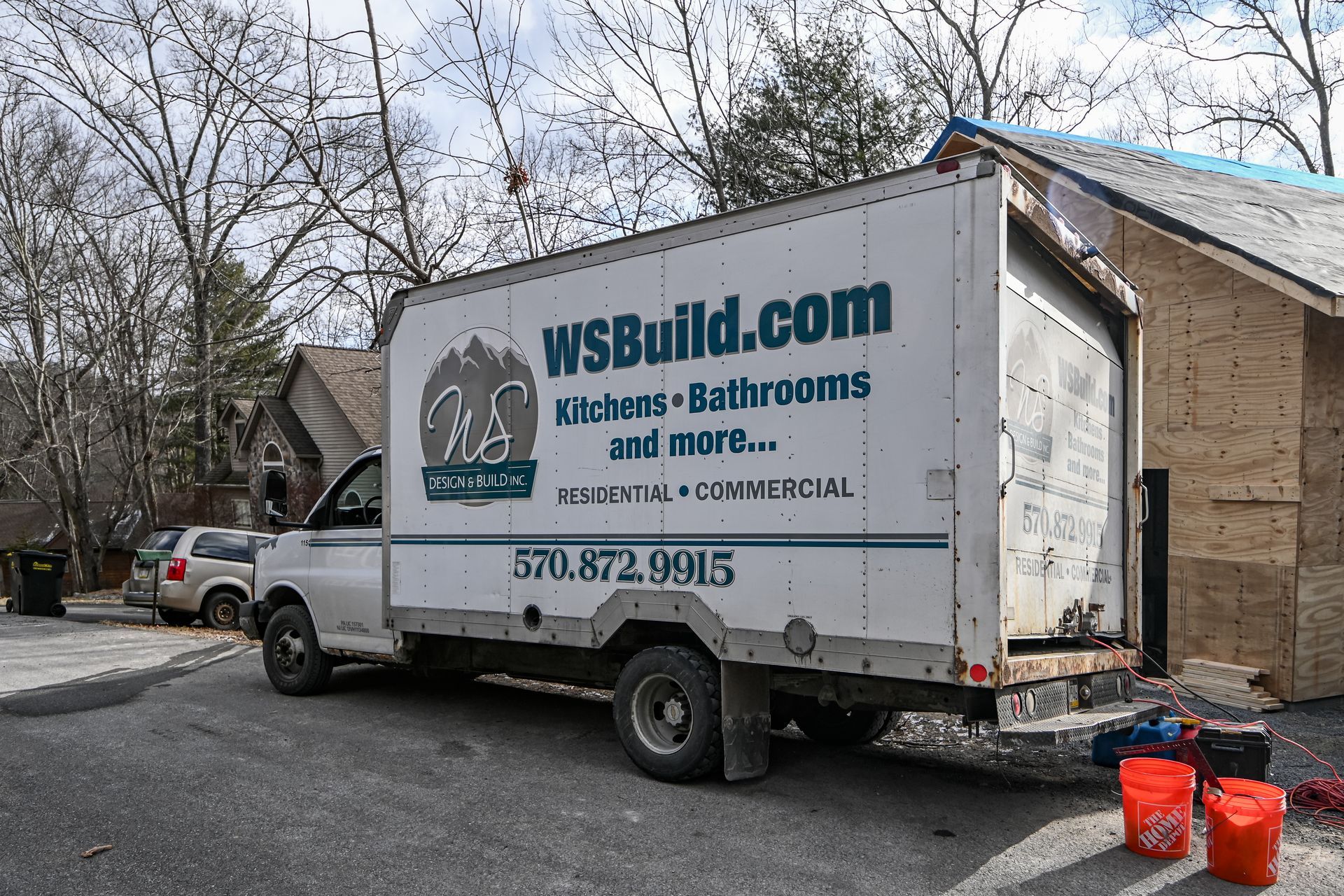 White WSBuild.com truck parked next to a house under construction; a few red buckets on the ground.