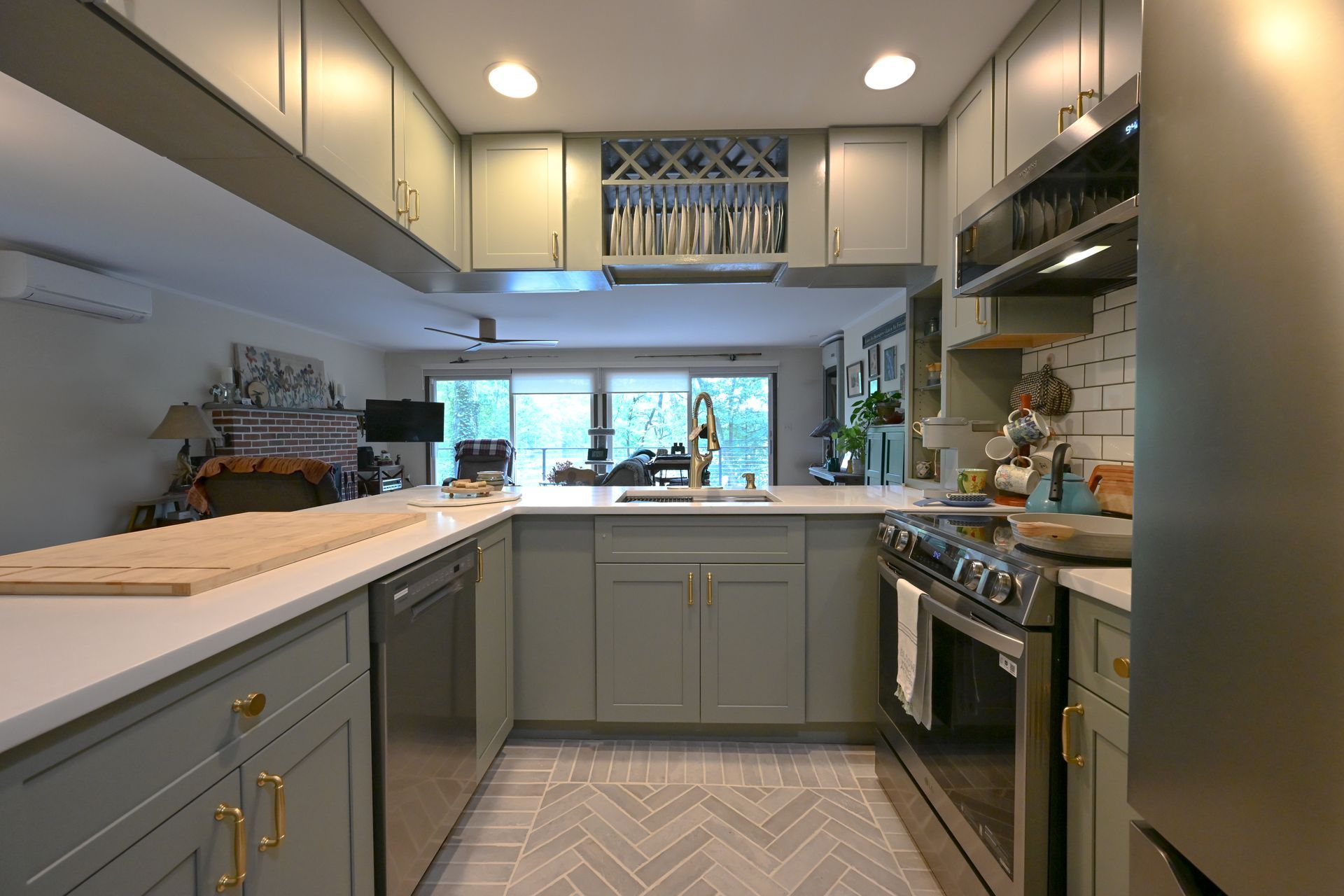 Modern galley kitchen with gray cabinets, marble counters, stainless stove, and a window over the sink