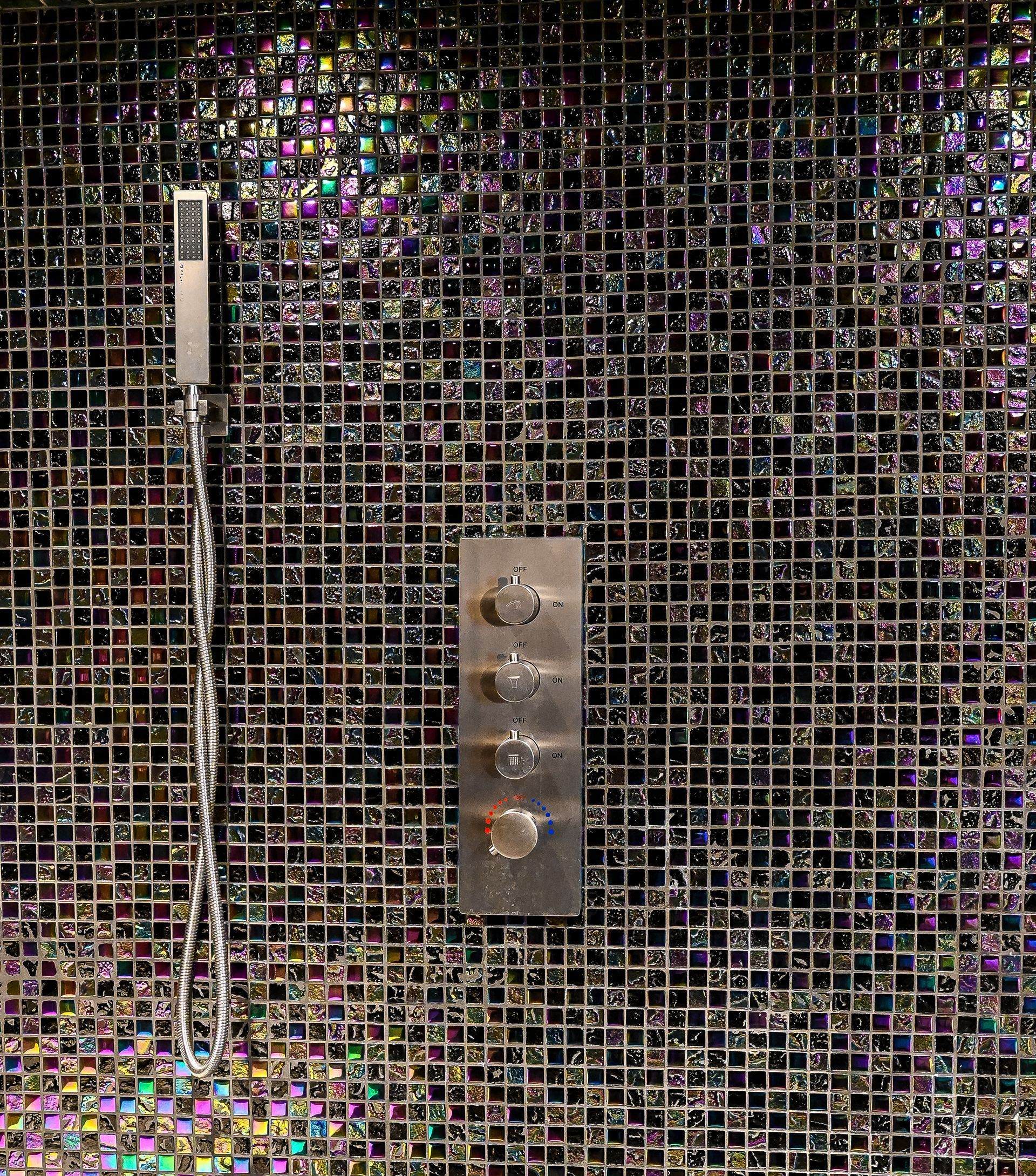 A shower head is hanging from a mosaic wall in a bathroom.