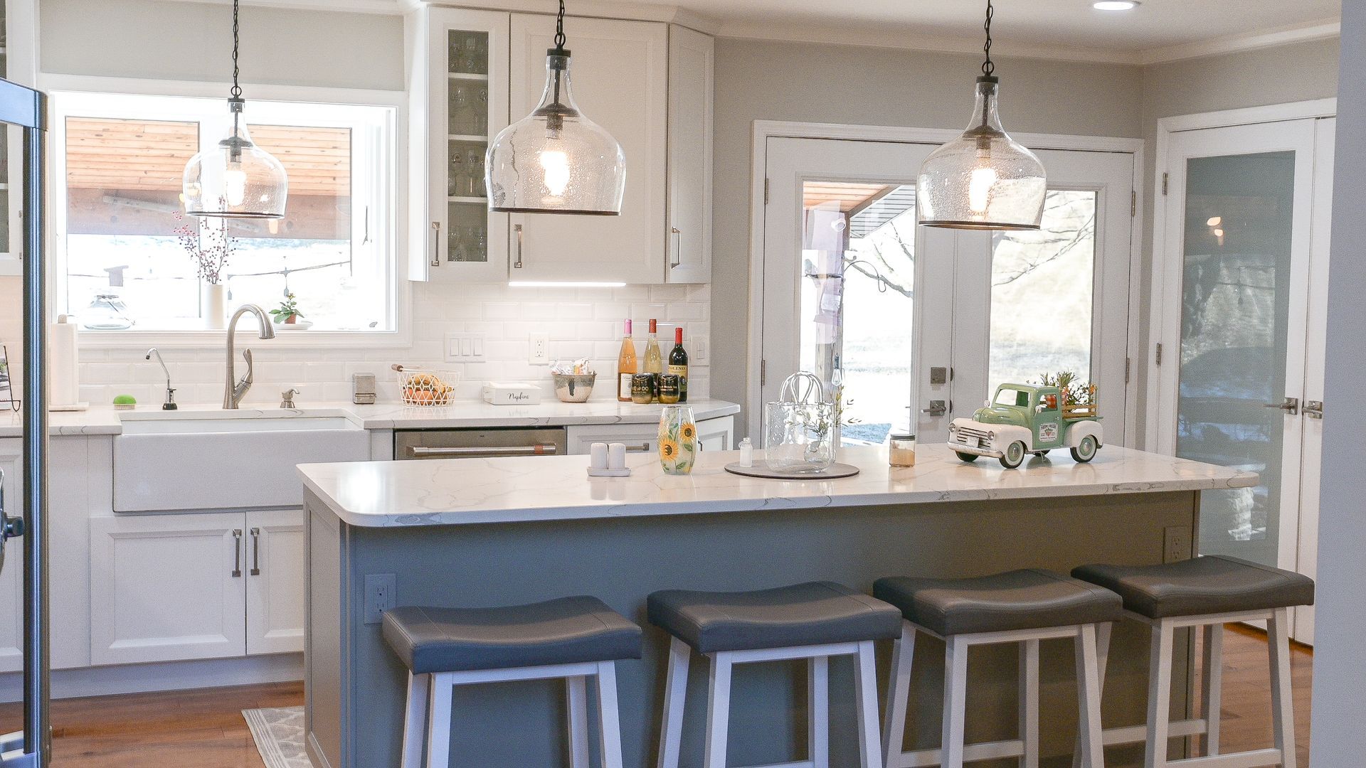 Bright modern kitchen with white cabinets, island, pendant lights, and stools by a window