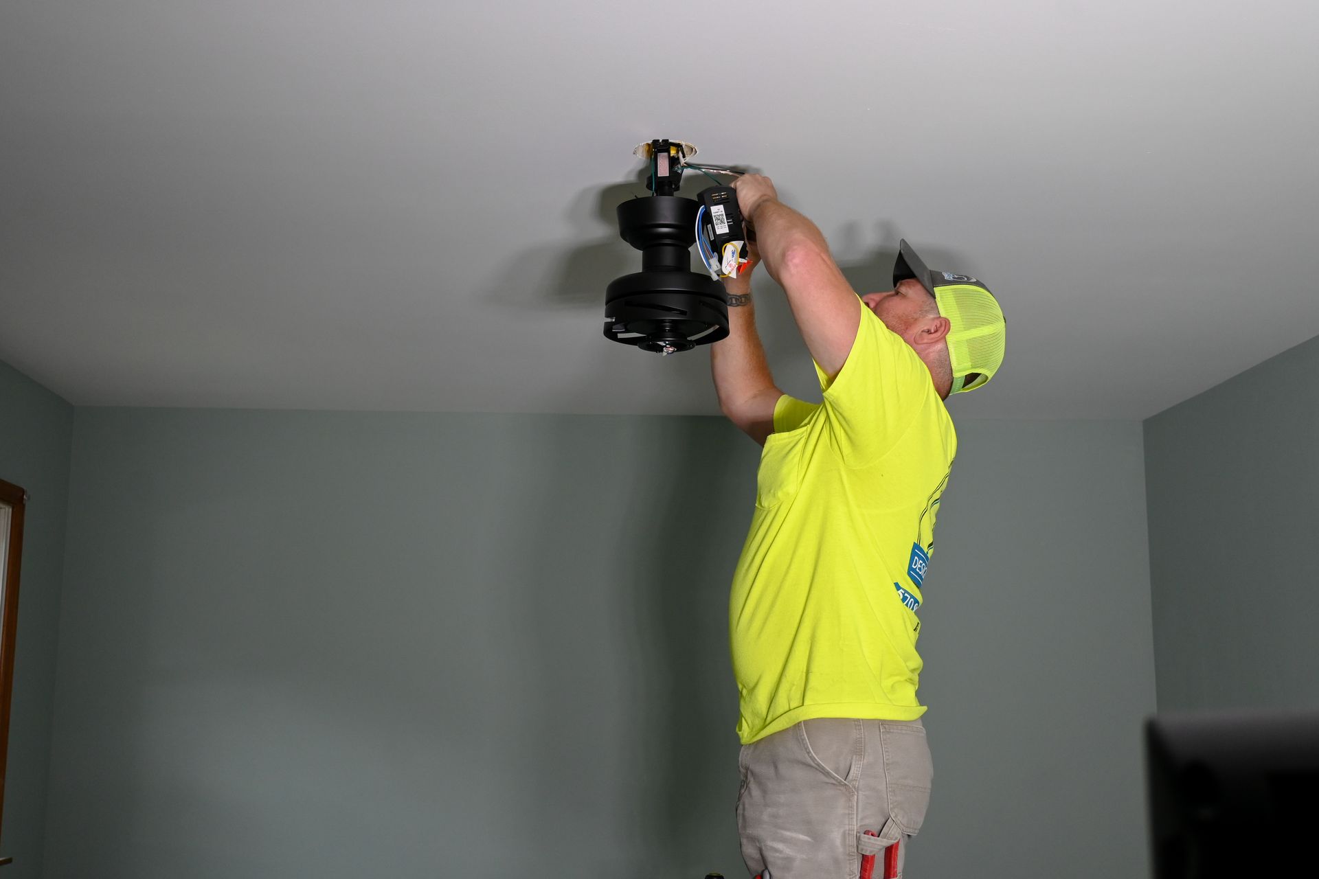 A man is installing a ceiling fan in a room.