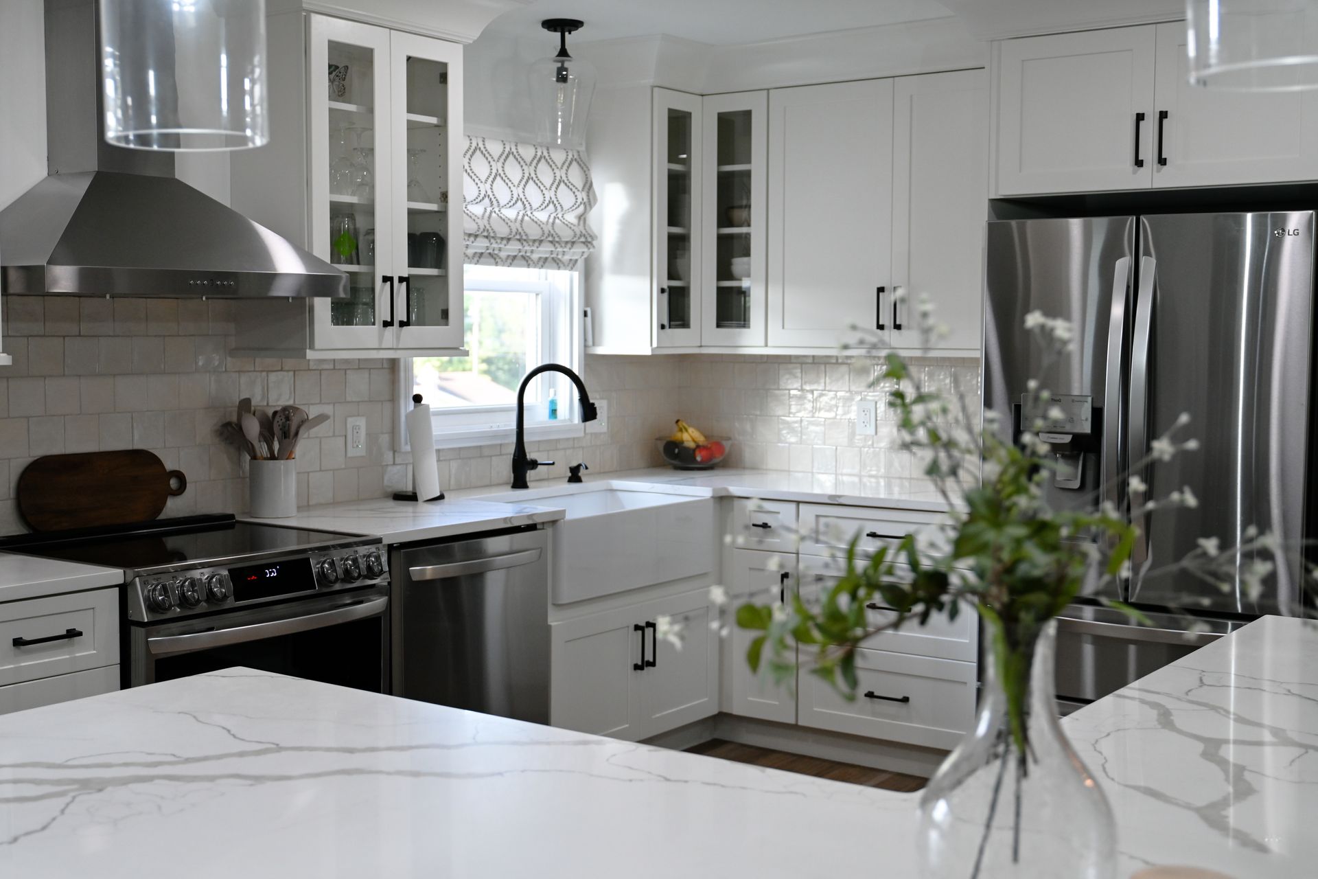 Bright white kitchen with stainless steel appliances, white cabinets, and a marble countertop.