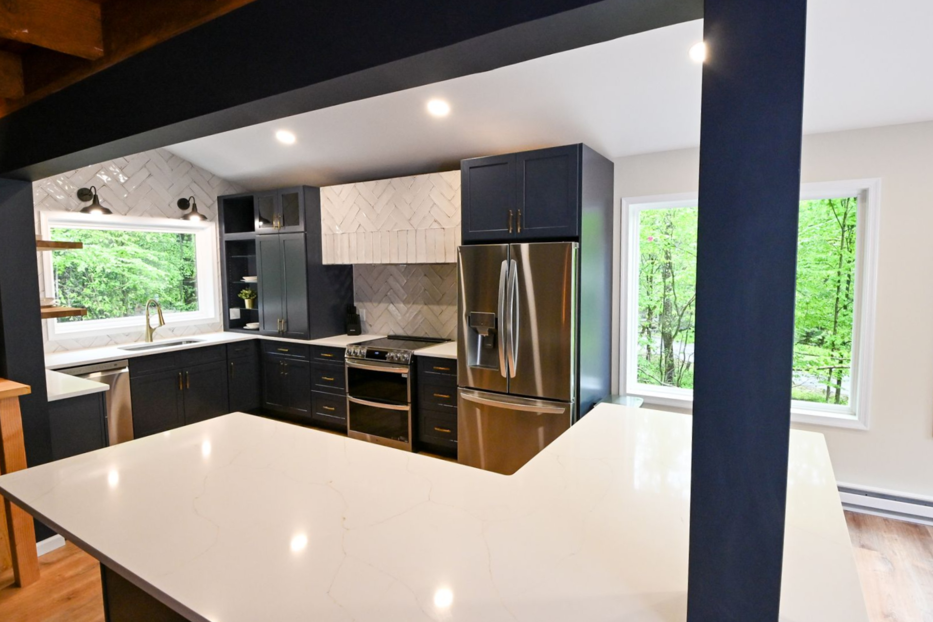 Modern kitchen with dark blue cabinets, stainless steel refrigerator, and white countertop.